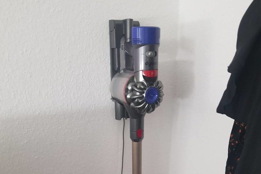 Getesteter Akku-Staubsauger der Marke Dyson steckt in der Ladestation, die in einem Flurbereich montiert ist.