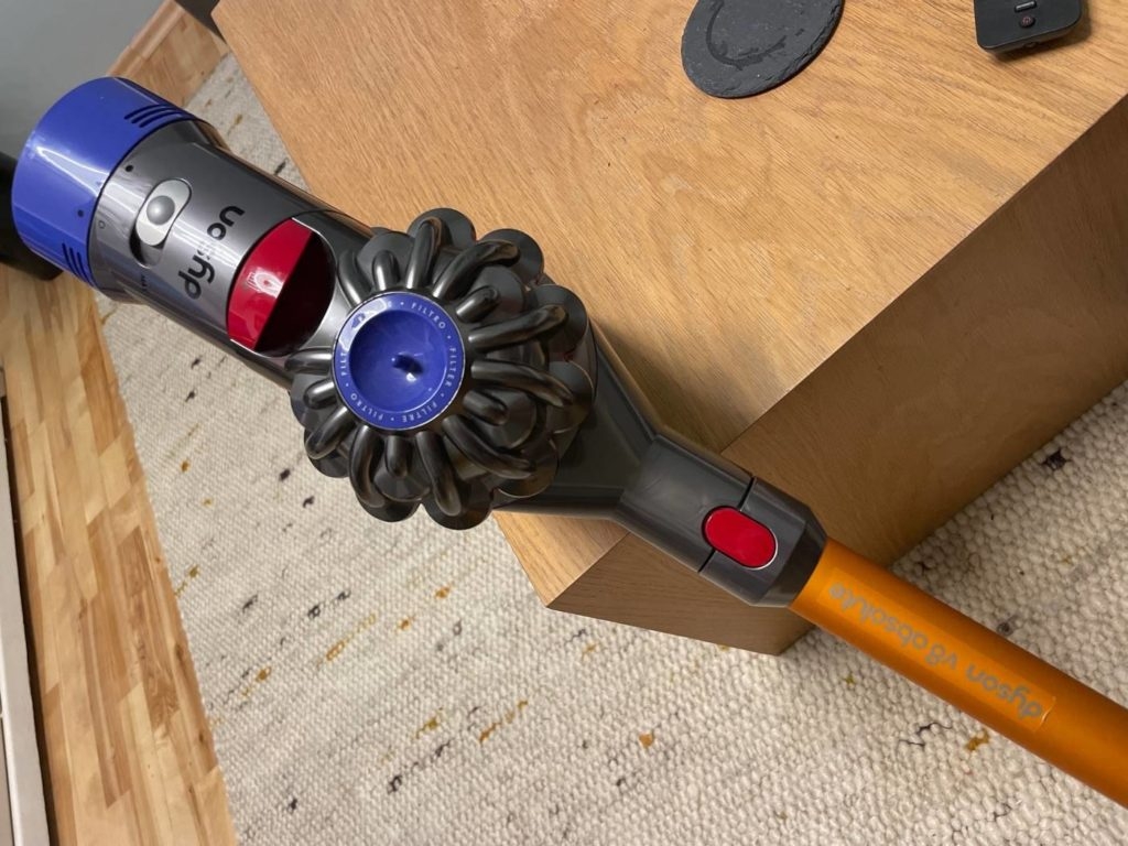 Nahaufnahme eines orangen Modells der Marke Dyson v8 absolute, der an einem Holzmöbel lehnt.