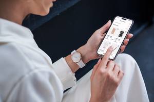 E-Commerce-Plattformen im Test: Eine Frau mit einer weißen Uhr am linken Handgelenk nutzt auf einem Smartphone einen Onlineshop.