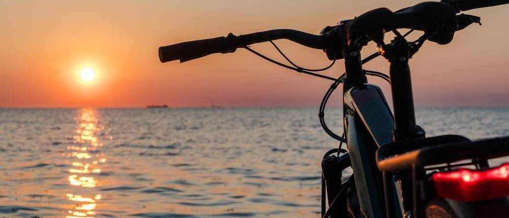 fahrradlampe-batterie-test: E-Bike steht bei Sonnenuntergang an einem Wasser