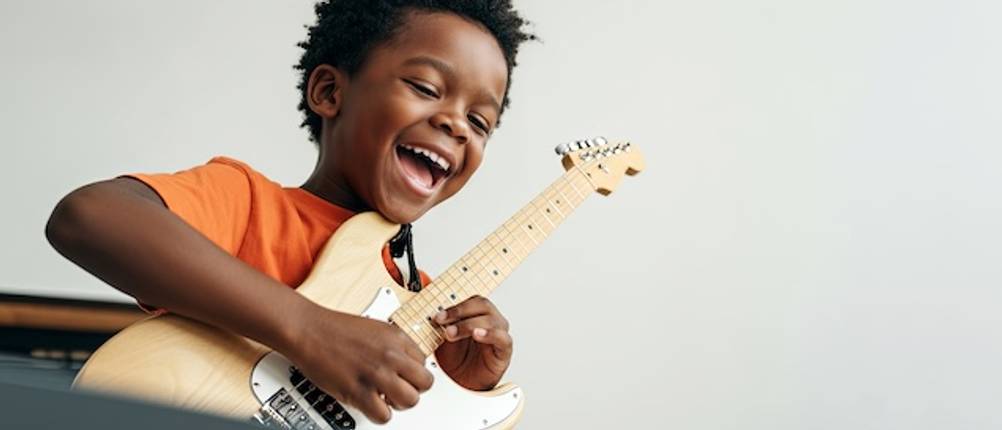 Kinder-E-Gitarren-Test: Ein Junge spielt auf einer weißen E-Gitarre und lacht dabei.