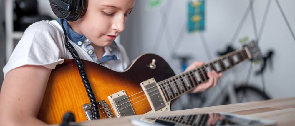 E-Gitarre-Kinder-Test: Ein Junge mit Kopfhörern übt auf einer E-Gitarre.