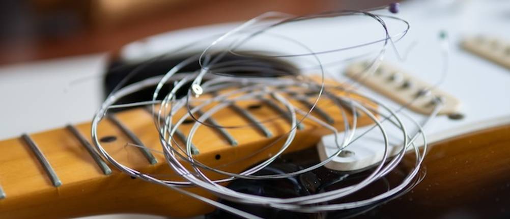 E-Gitarren-Saiten-Test: Benutzte E-Gitarren-Saiten liegen zusammengerollt auf dem Griffbrett einer E-Gitarre.