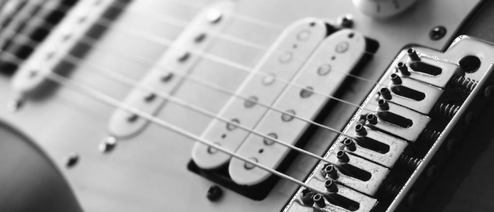 Getestete E-GItarren-Saiten als Schwarz-Weiß-Nahaufnahme am Steg einer E-Gitarre.
