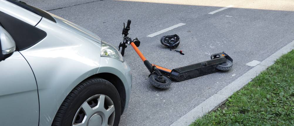 Ein E-Roller liegt nach einem Unfall vor einem einem Auto.