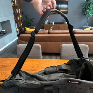 Eine Hand hebt den Tragegurt der Eastpak TERMINAL-+-Reisetasche hoch