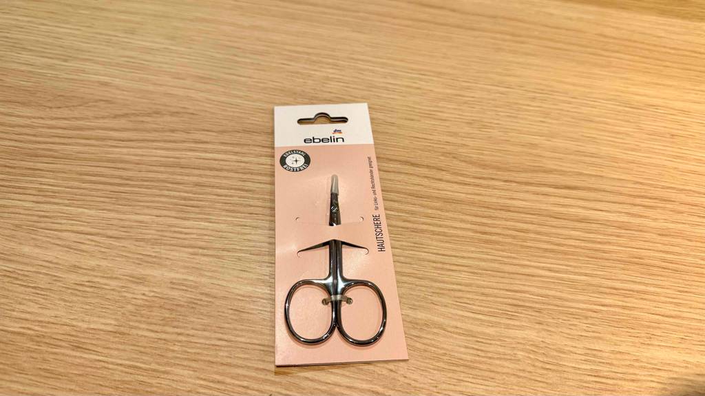 Eine getestete Hautschere liegt verpackt auf einer Holzfläche.