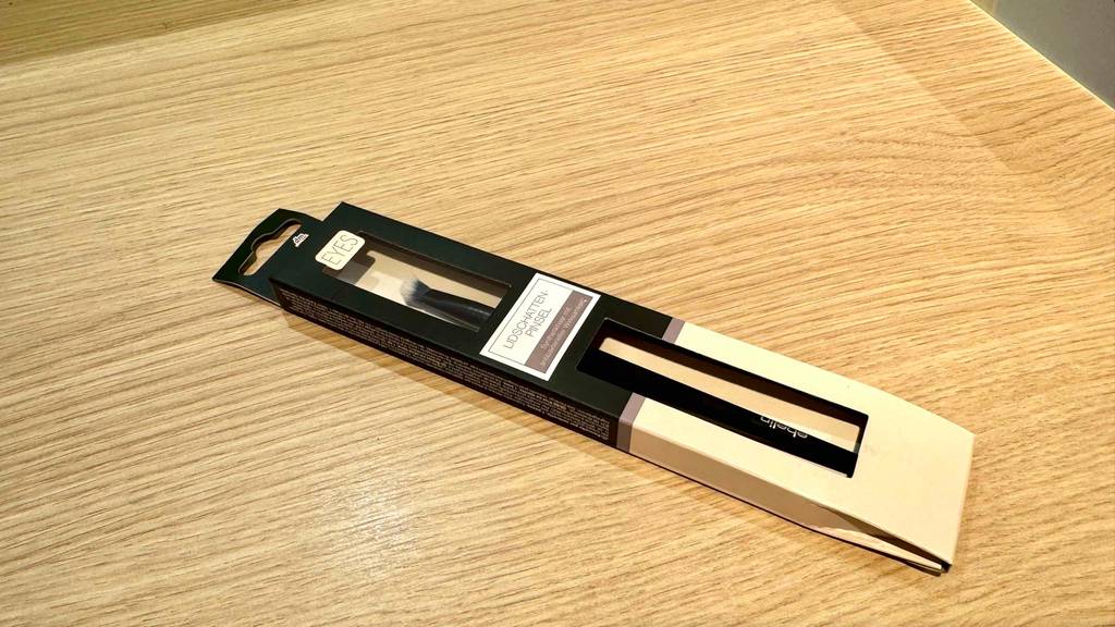 Eine Packung mit einem getesteten Lidschattenpinsel liegt auf einer Holzfläche.