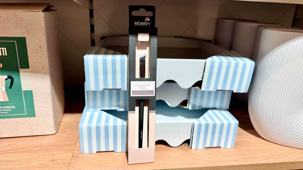 Im Test: Ein Lidschattenpinsel steht in Originalverpackung vor Kartons in einem Regal.