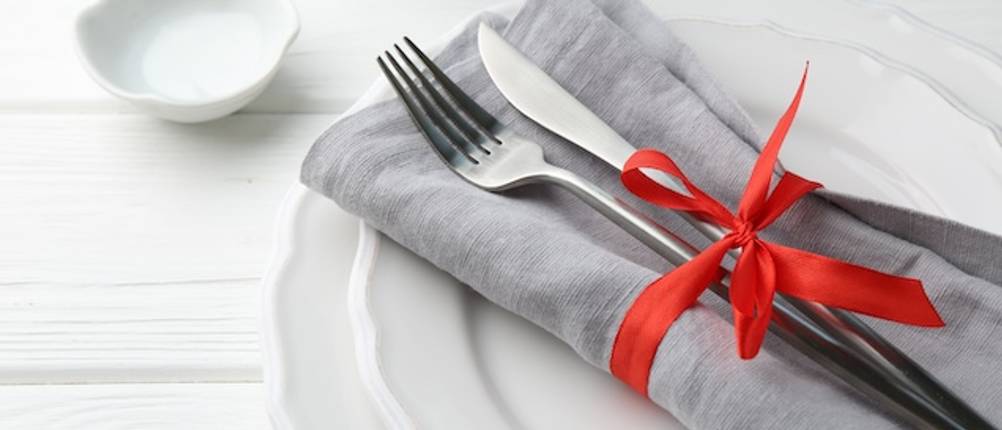 Echtwerk-Besteck getestet: Messer und Gabel liegen auf einer grauen Serviette, gehalten von einem roten Band, auf einem weißen Teller.