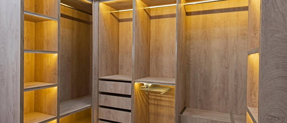 Eckkleiderschrank-Test: Ein beleuchteter Eckkleiderschrank aus Holz füllt einen Raum vollständig aus.