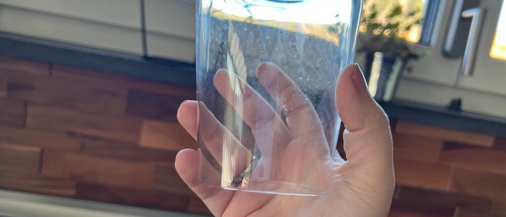 Eine Hand hält ein Glas mit leichten Verschmutzungen gegen das Licht
