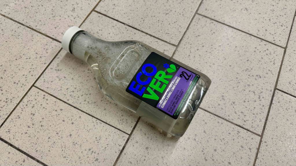 Eine Glasflasche mit getestetem Waschmittel für schwarze Wäsche liegt auf einem Fliesenboden.