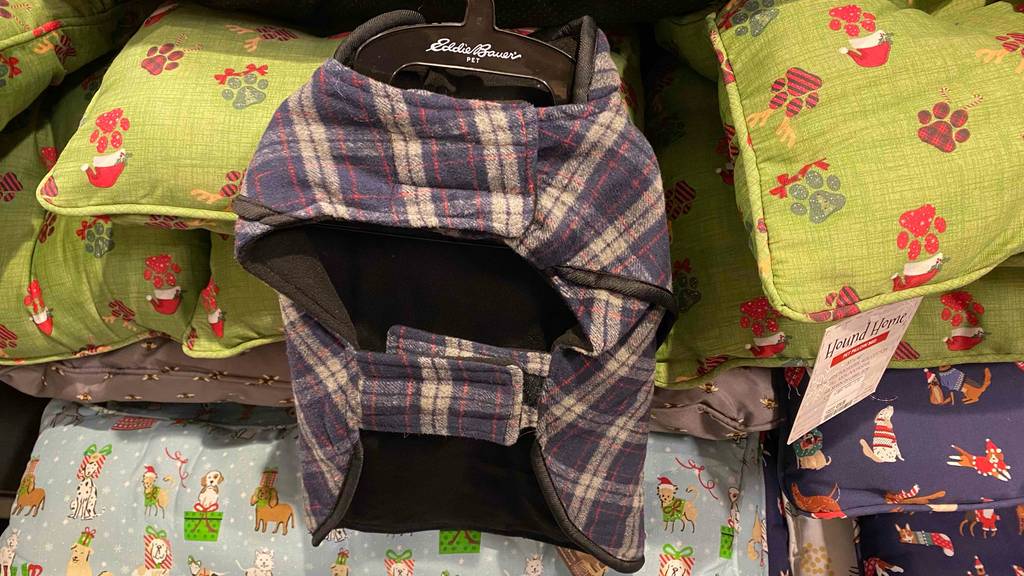 Ein Eddie Bauer PET Hundemantel im Test befindet sich auf einem Kleiderbügel auf mehreren bunten Hundekissen.