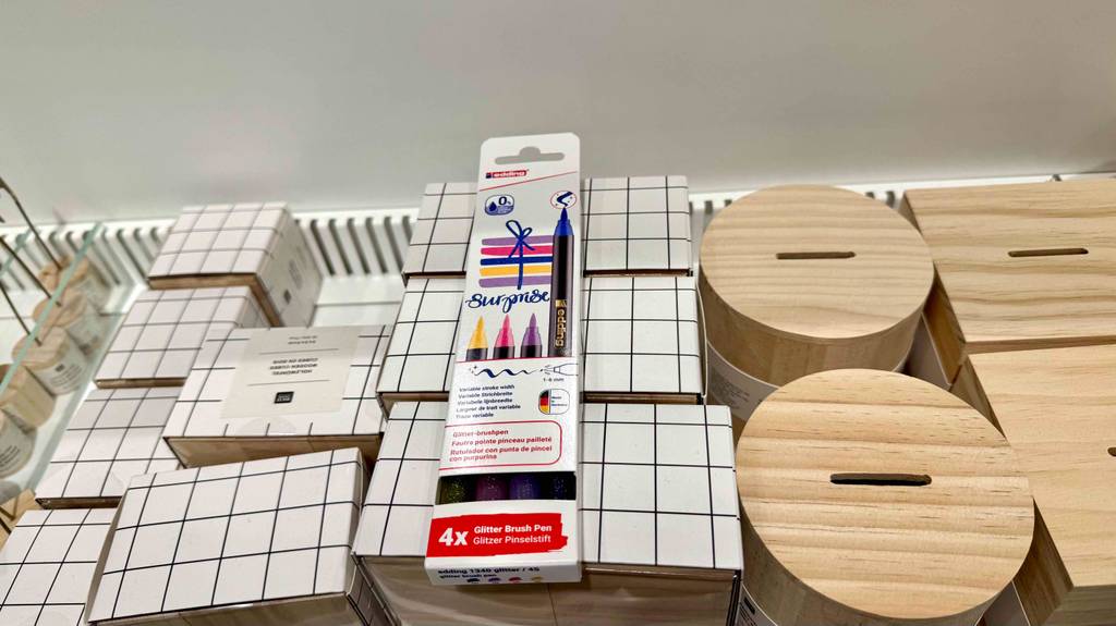 Die Pinselstifte im Test liegen innerhalb einer Vierer-Packung auf mehreren Bastel-Produkten aus hellem Holz und Karton.