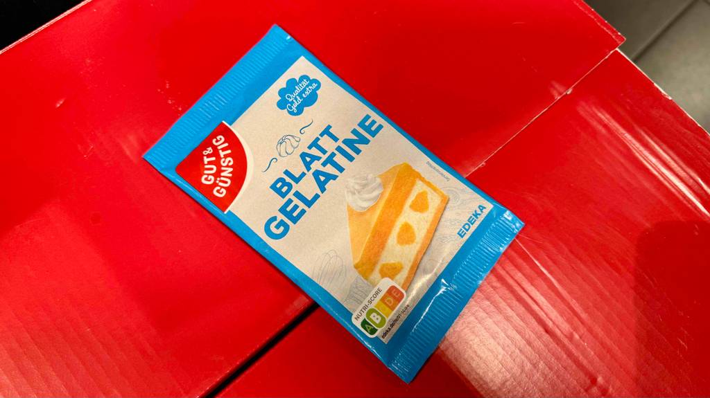 Eine Packung Blatt-Gelatine liegt zum testen auf einem roten Karton.