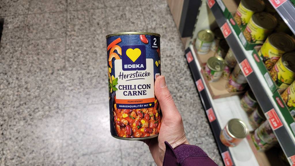 Eine Hand hält die Dose mit getestetem Chili con Carne neben einem Verkaufsregal.