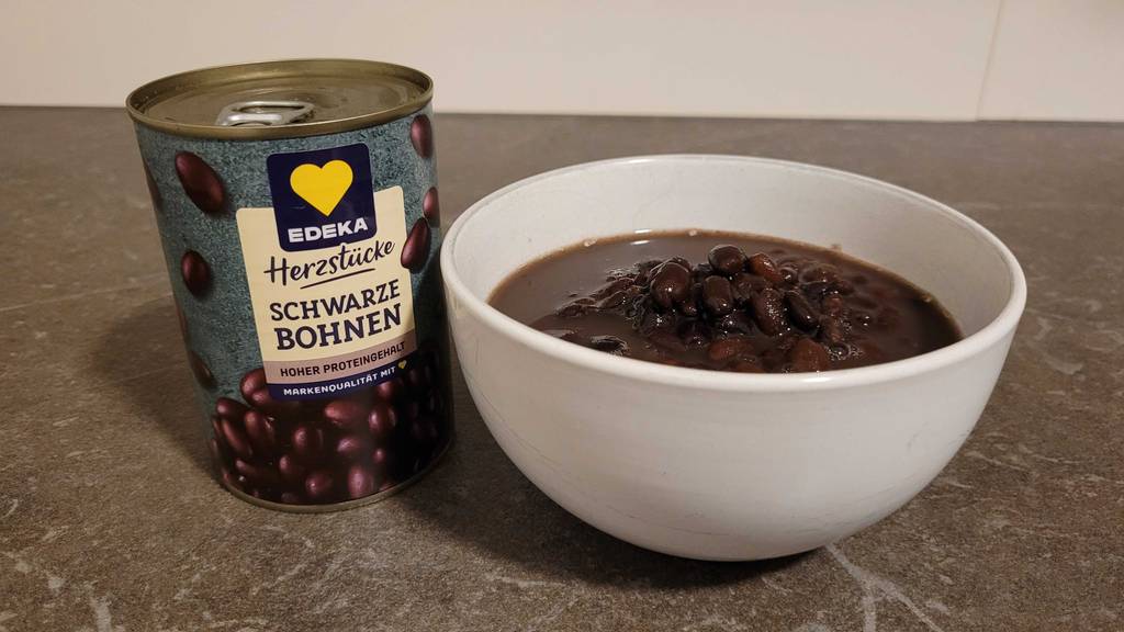 Neben einer weißen Schüssel mit getesteten schwarzen Bohnen steht eine verschlossene Büchse schwarze Bohnen.