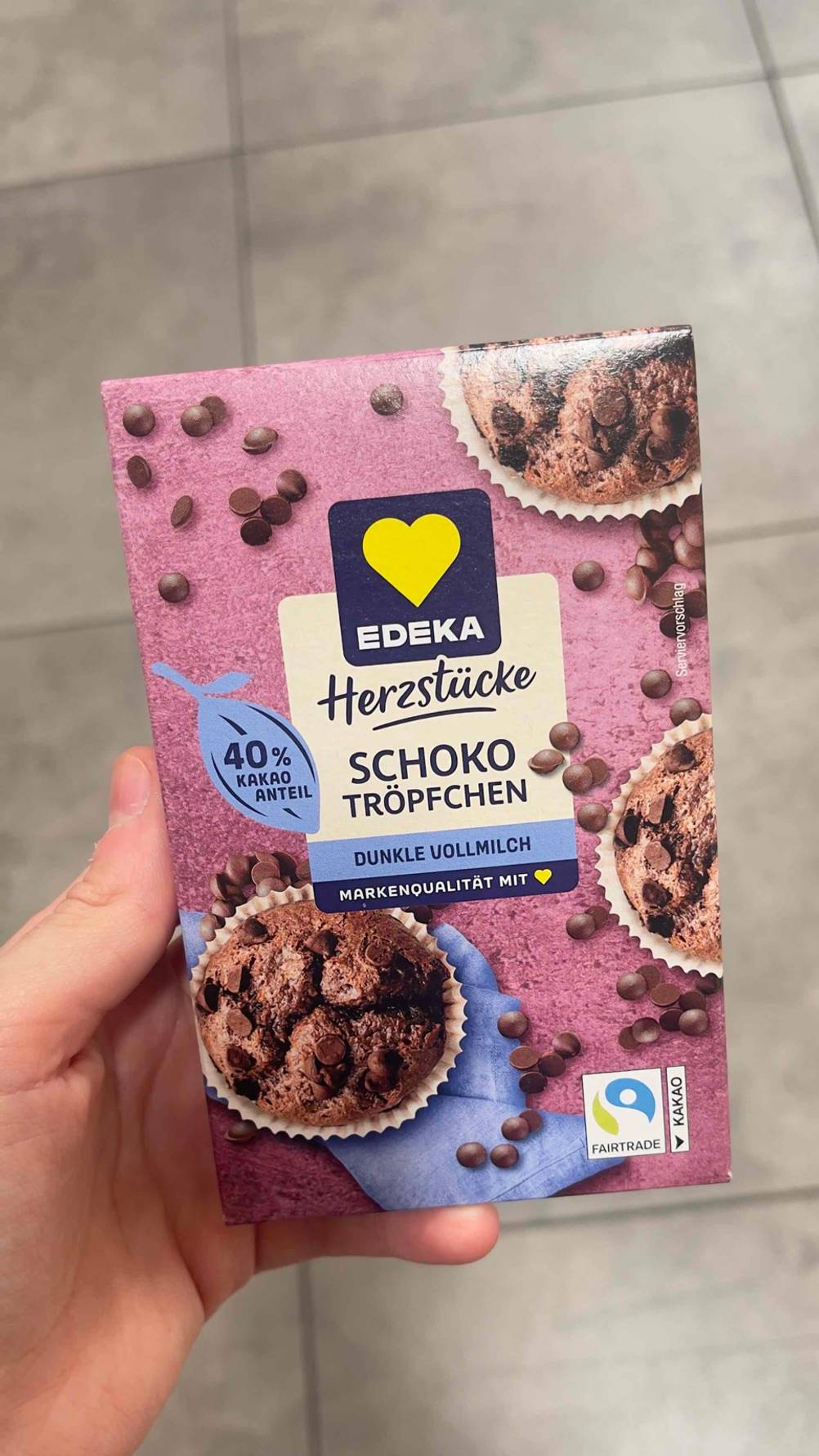 Im Test: Die Schokodrops der Marke EDEKA in der Packung, die sich in einer Hand über einem grauen Fliesenboden befindet.