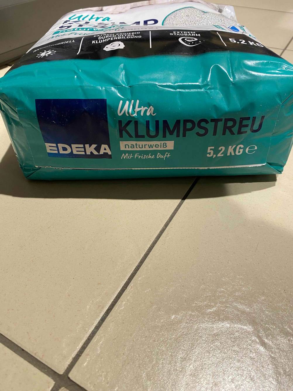 Getestet: Nahaufnahme des Bodens einer Packung Katzenstreu auf einer hellen Fließenfläche.