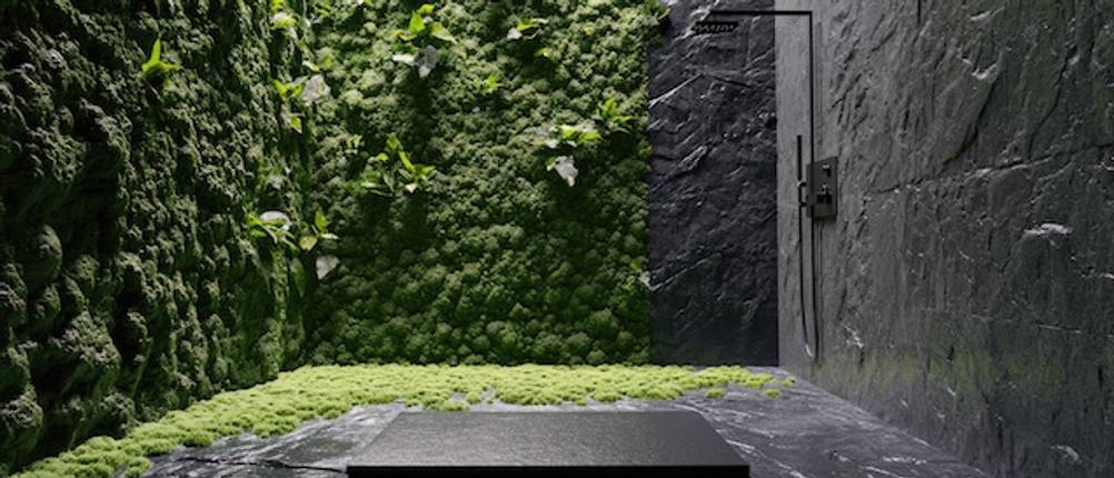 Edelstahl-Gartenduschen-Test: Eine schwarze Gartendusche an einer dunkelgrauen Granitwand mit Bodenplatte in einem Garten mit hoher grüner Hecke.