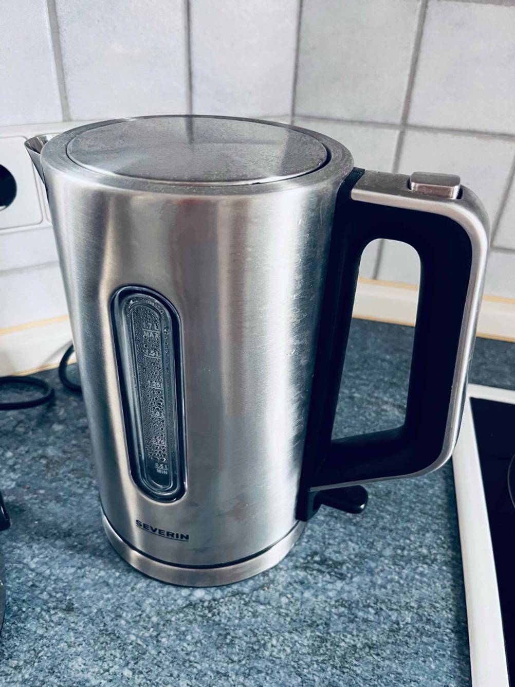 Seitenansicht eines getesteten Edelstahl-Wasserkochers auf einer blauen Arbeitsfläche.