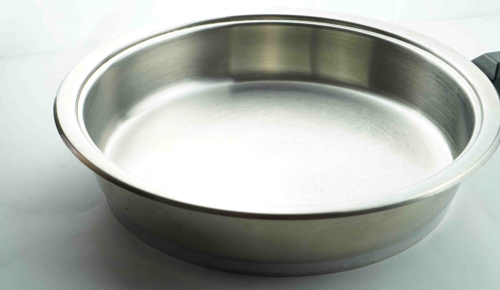 Nahaufnahme der Innenfläche einer getesten Edelstahlpfanne auf einer hellen Fläche.