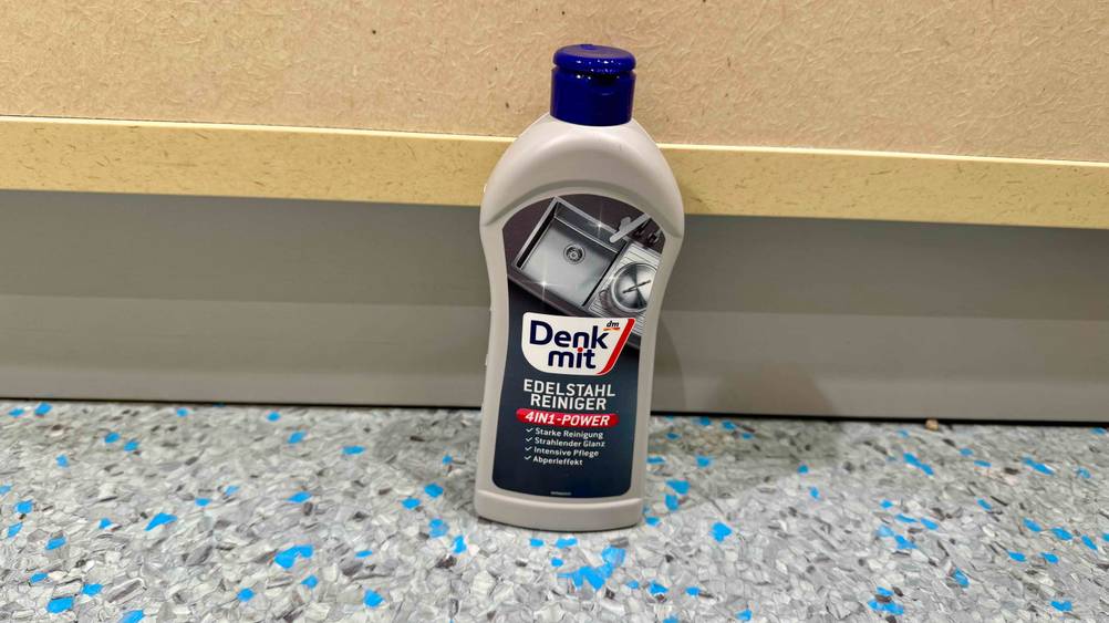 Der getestete Edelstahlreiniger am Boden vor einem Schrank.