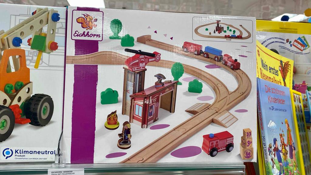 Holzeisenbahn im Test: Eine bunte Verpackung mit einer Holzeisenbahn von Eichhorn befindet sich inmitten von Kinderspielzeug.