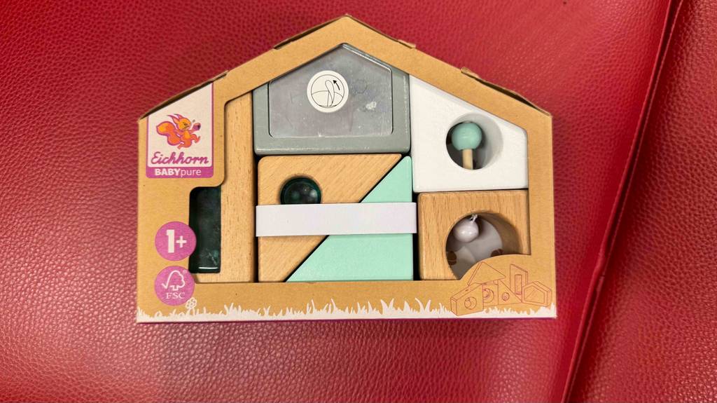 Ein verpacktes Holzspielzeug für das Baby liegt zum testen auf einer roten Fläche.