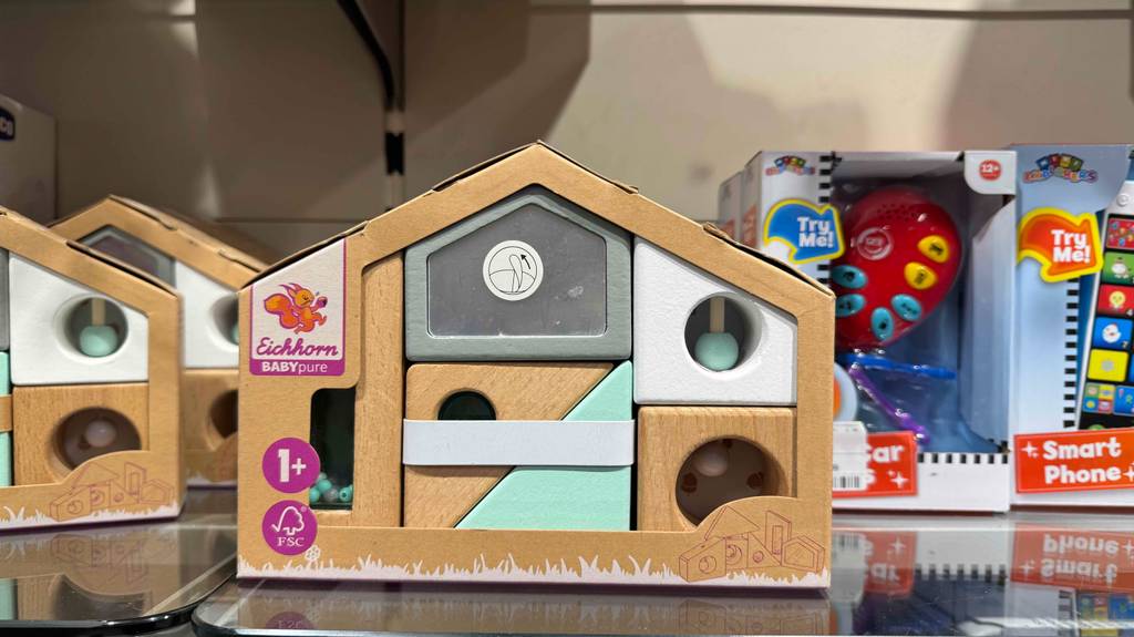 Holzspielzeug für das Baby im Test: Ein Holzbauhaus steht zwischen anderen Spielprodukten in einem Regal.