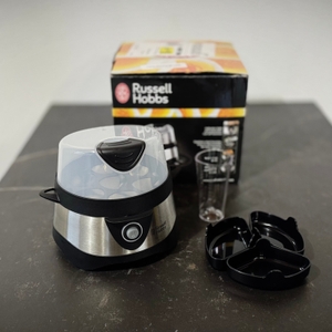 Die Verpackung des getesteten Eierkochers von Russell Hobbs steht zusammen mit den Pochierschalen auf einer dunklen Arbeitsfläche.