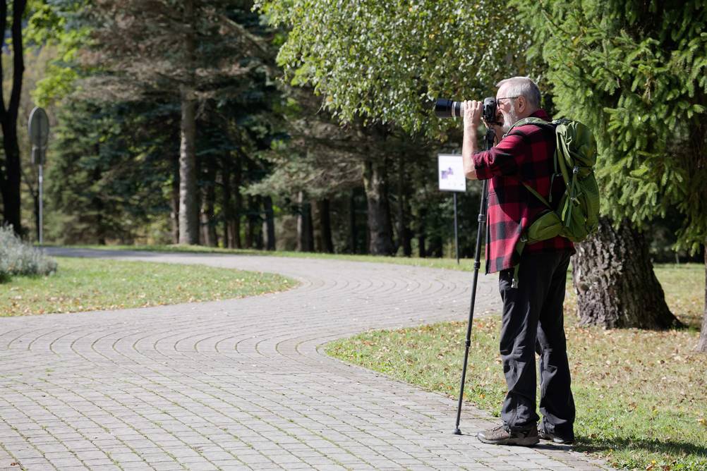 Einbeinstativ im Test: Ein Mann steht am Rande eines Waldes oder Parks mit einer Kamera und einem Einbeinstativ.