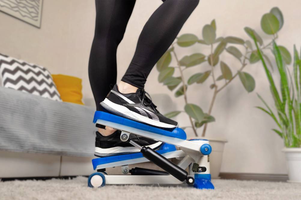 Sportgeräte für zuhause im Test: Eine Frau trainiert auf einem Stepper. Man sieht nur die Beine. Sie trägt eine schwarze Sporthose und schwarze Sneaker.