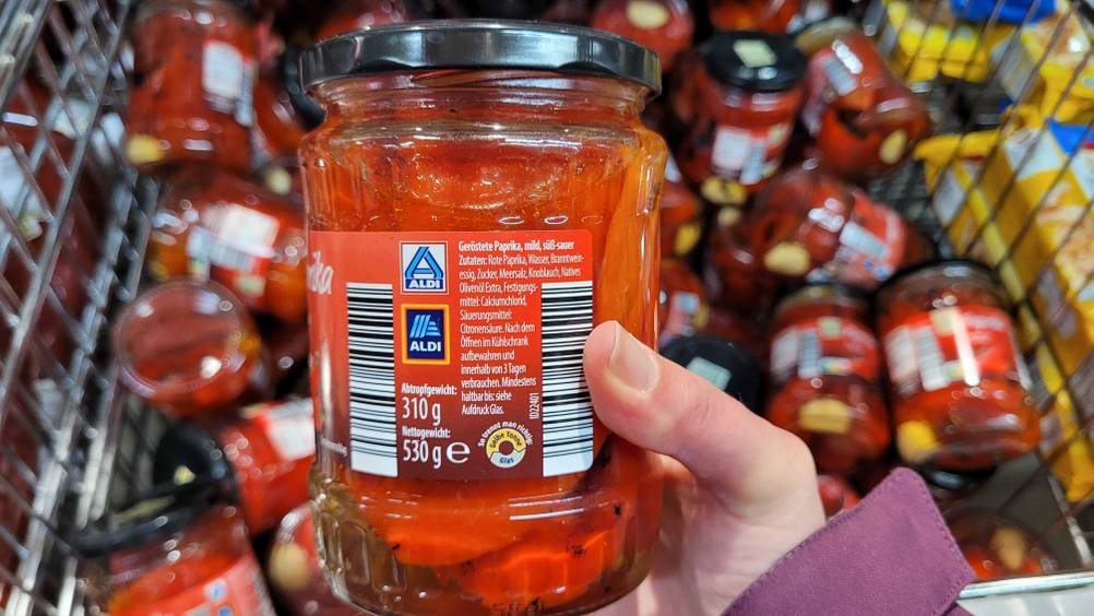 Eine Hand hält ein Glas der eingelegten Paprika hoch.
