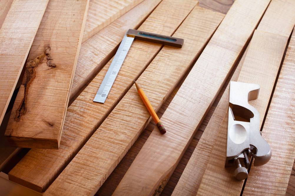 Einhandhobel im Test: Auf einem Stapel Bretter liegen ein Metallwinkel, ein Bleistift und ein kleiner Einhandhobel