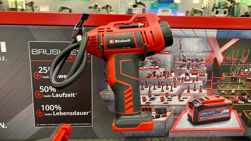 Im Test: Eine Akku-Luftpumpe von der Seite vor einem Plakat der Marke Einhell.