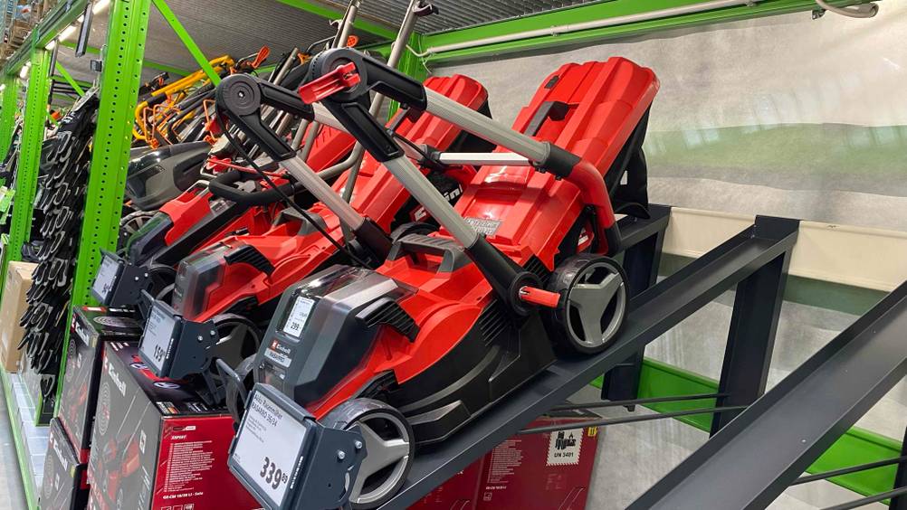 Ein getesteter Einhell-Akku-Rasenmäher schräg von der Seite mit Preisangabe, im Hintergrund andere Produkte.