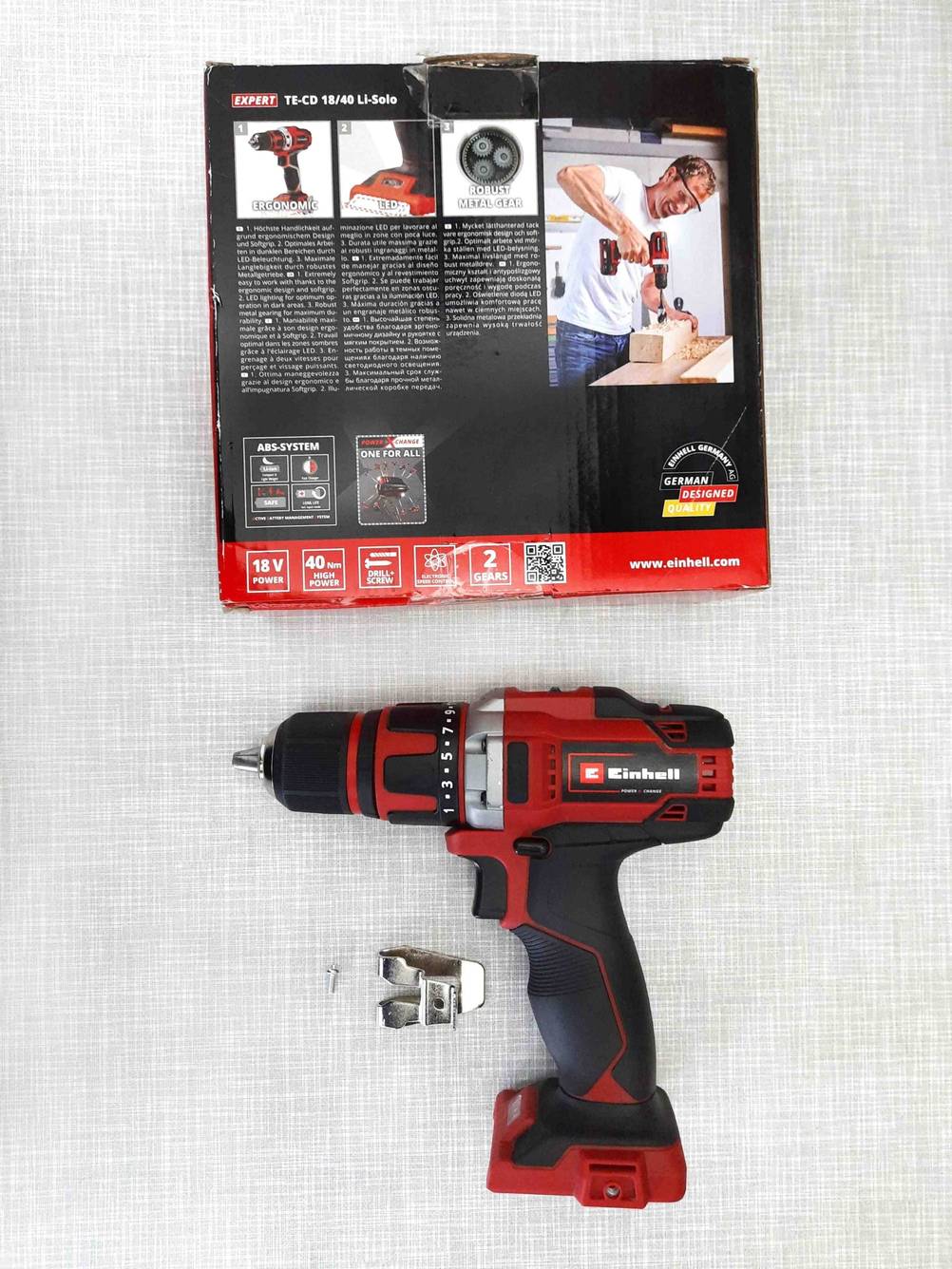 Im Test: Über einem Einhell-Akkuschrauber 18V liegt eine Originalverpackung mit der Rückseite nach oben auf einer grauen Fläche.