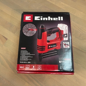 Einhell Akku-Tacker TE-CN 18 Li in Originalverpackung auf hellem Holzboden fotografiert. Die Verpackung zeigt Gerät, Herstellerlogo und technische Merkmale.