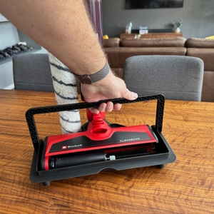 Ein Hand hebt den Halter des Einhell CLEANEXXO am Traggriff hoch