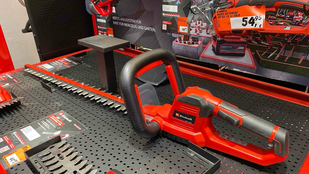 Im Test: eine Einhell-Heckenschere im roten Design, inklusive langem Sägeblatt und großem Haltegriff befindet sich auf einem Verkaufsregal.