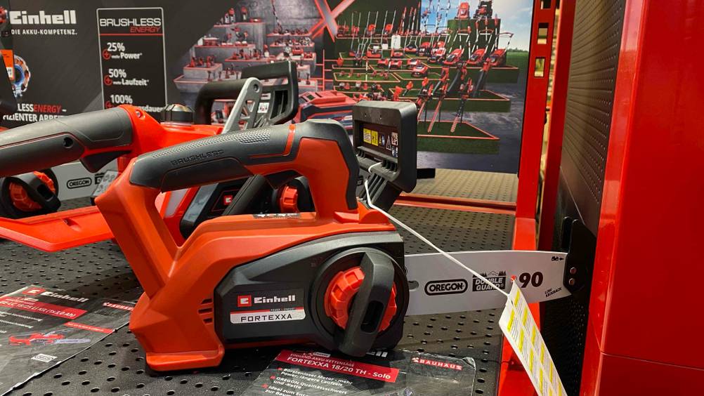 Eine Kettensäge von der Seite in einer Verkaufsfläche neben anderen Produkten stehend.