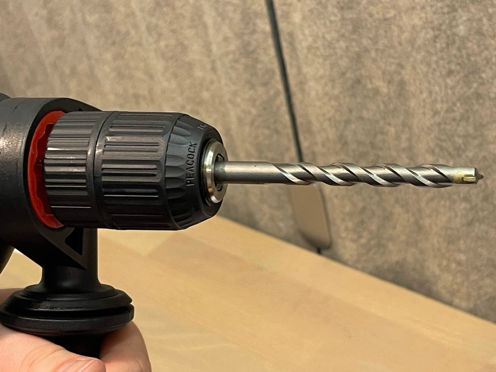 Die Einhell-TC-ID-720/1-E-Schlagbohrmaschine mit eingespanntem Bohrer in Seitenansicht. Der Zusatzgriff ist gut sichtbar.