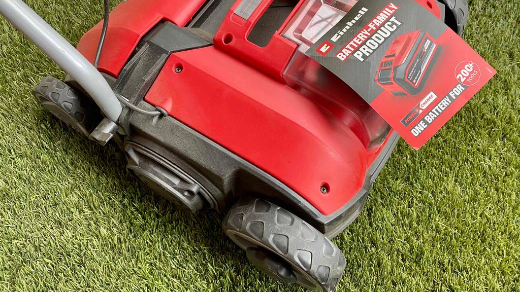 Im Test: Einhell Akku Vertikutierer steht auf einem Rasen mit Anleitung obenliegend.