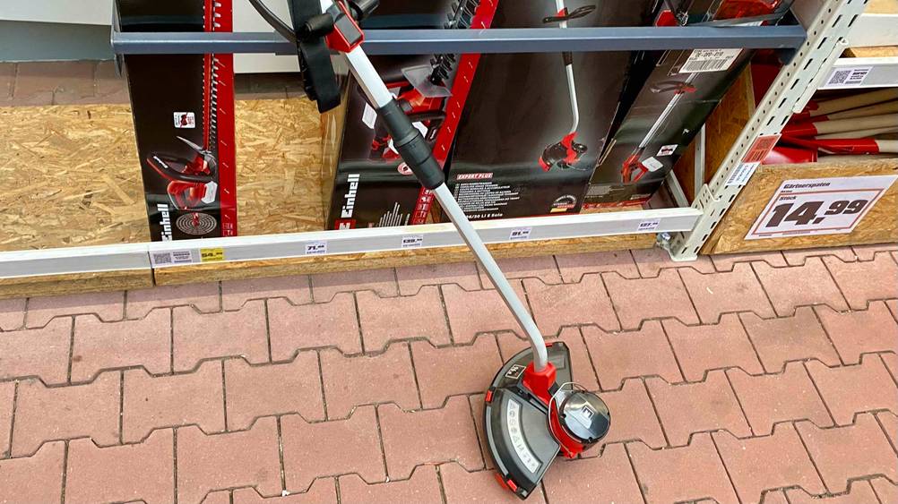 Ein Einhell-Rasentrimmer im Test lehnt an einem Regal in einem Baumarkt.