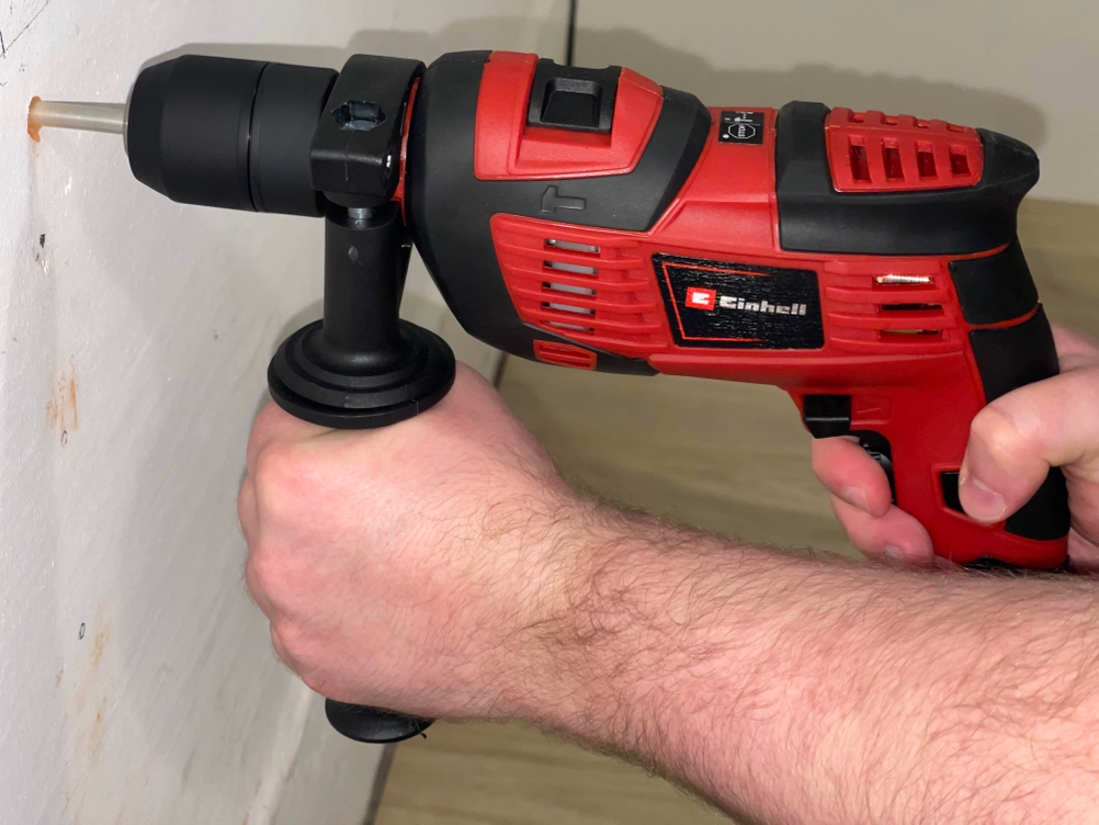 Die Einhell TC-ID 720/1 E im Einsatz beim Bohren in eine weiße Wand. Zwei Hände halten das Gerät stabil.
