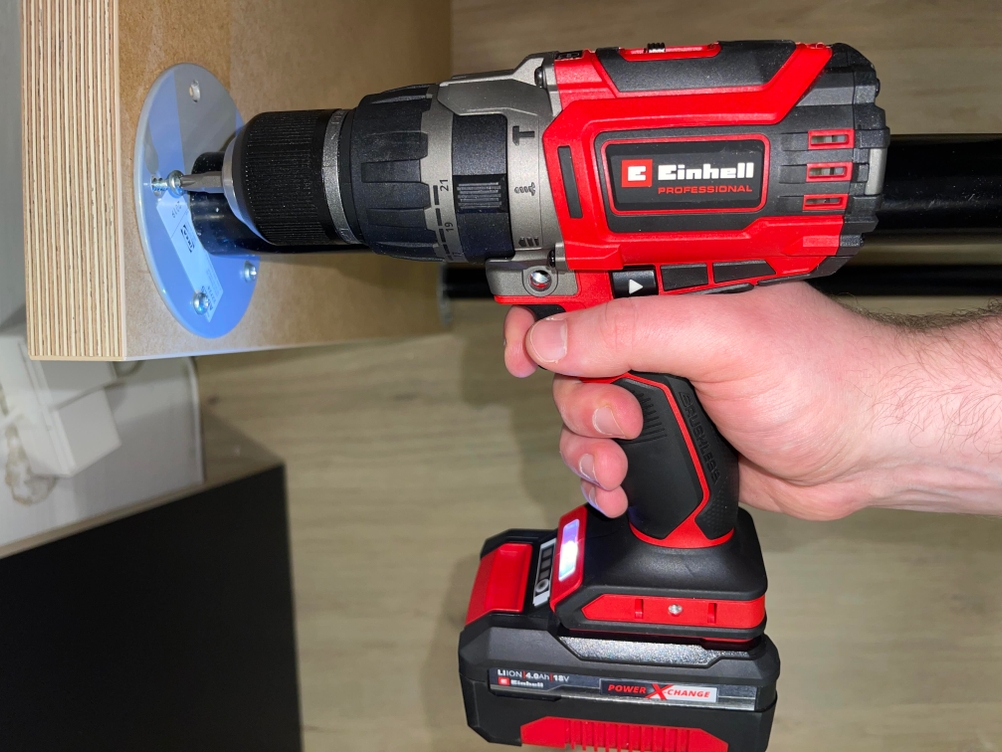 Einhell Professional Akku-Schlagbohrschrauber wird zum Verschrauben in eine Tischplatte eingesetzt. Die Hand führt das Gerät waagerecht mit sichtbarer LED-Beleuchtung.