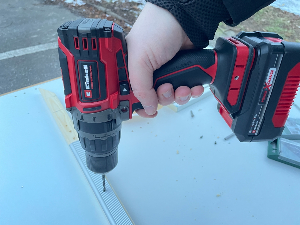 Das Bild zeigt den Einhell Professional TP-CD 18/70 Li BL beim präzisen Bohren in eine beschichtete Platte. Eine Führungsschiene liegt als Orientierung auf dem Werkstück.