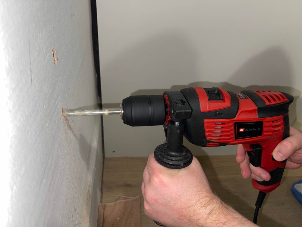 Die Einhell TC-ID 720/1 E bohrt mit montiertem Bohrer horizontal in eine weiße Wand. Die Maschine wird beidhändig geführt.